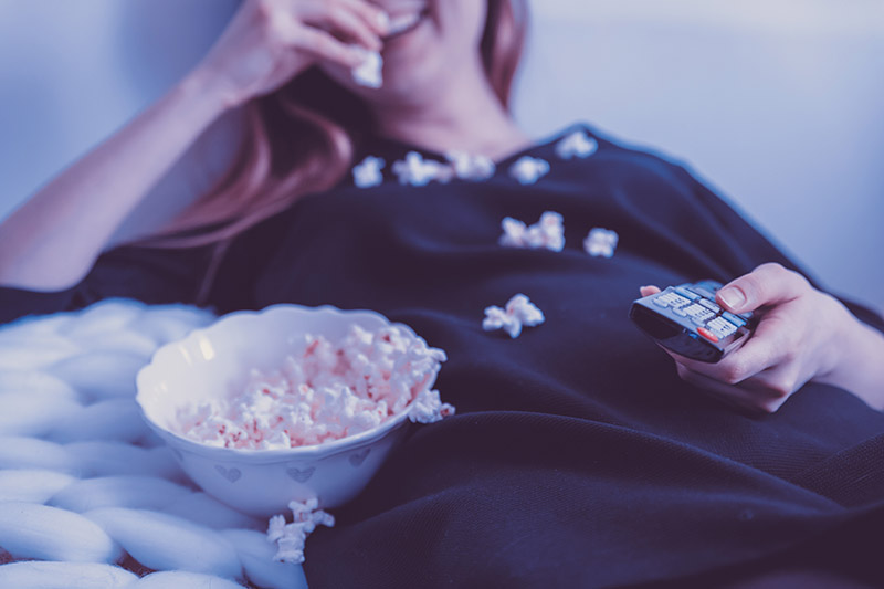 woman holding a remote with a bowl of popcorn spilled on her black shirt