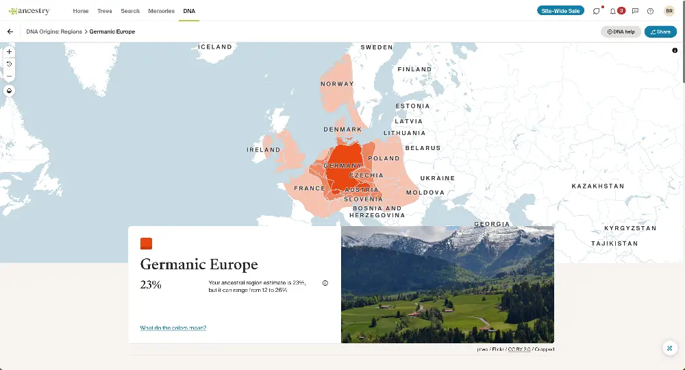 Alt text: A DNA ancestry map highlighting the Germanic Europe region, shaded in orange, with an ancestral estimate of 23% for this area, ranging from 12% to 26%. The highlighted regions include Germany, parts of Austria, Denmark, Switzerland, and surrounding countries. Below the map, a photo showcases a scenic alpine landscape with green fields, trees, and snow-capped mountains in the background.