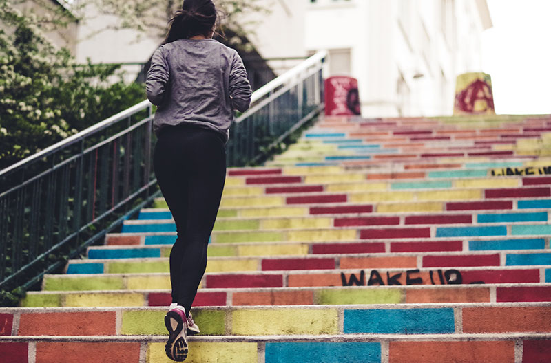woman running up rainbow-painted stairs | train for hiking