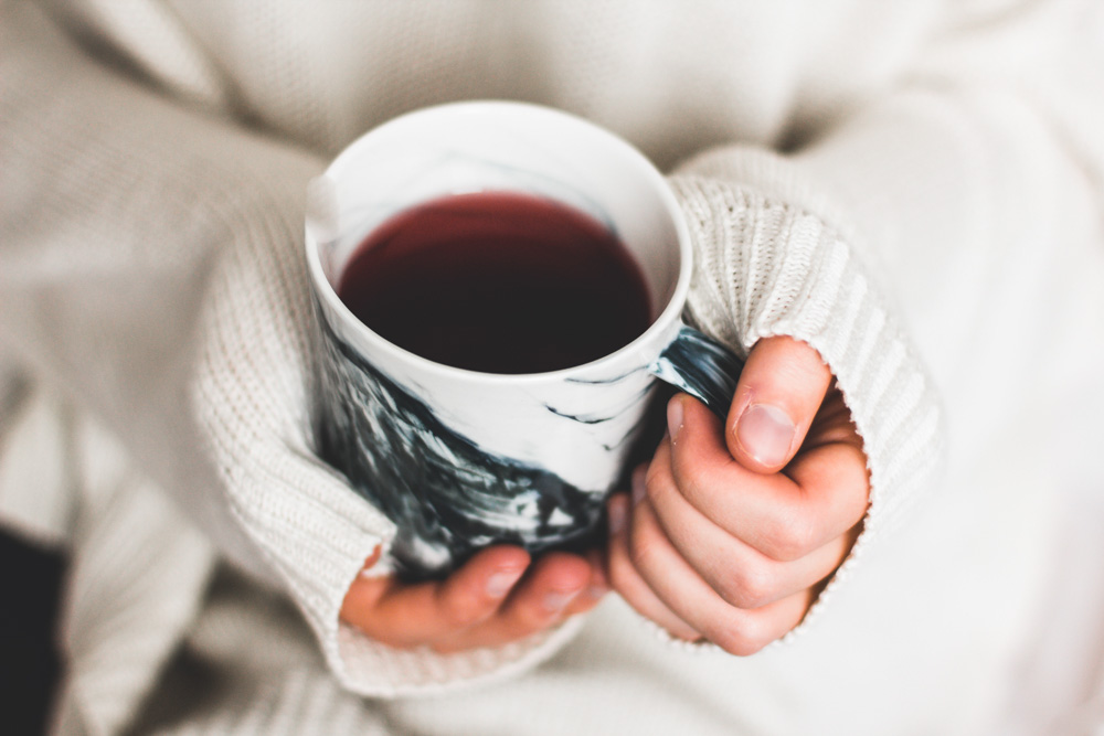 A person wearing a cream-colored knit sweater holding a black and white marble mug full of tea. winter hygge songs
