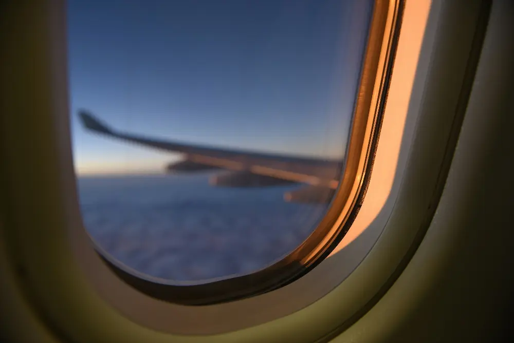 View from an airplane window during flight, showing a blurred airplane wing against the backdrop of a golden sunset and a sea of clouds below. travel with a purpose